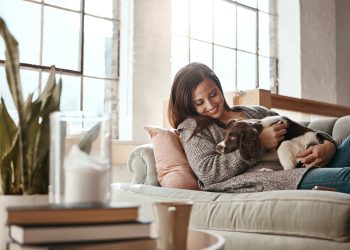 Woman relax on couch with puppy, happy and content at home with pet, happiness together with peace in living room. .Female cuddle dog, love for animals with smile and care, stress relief and comfort.